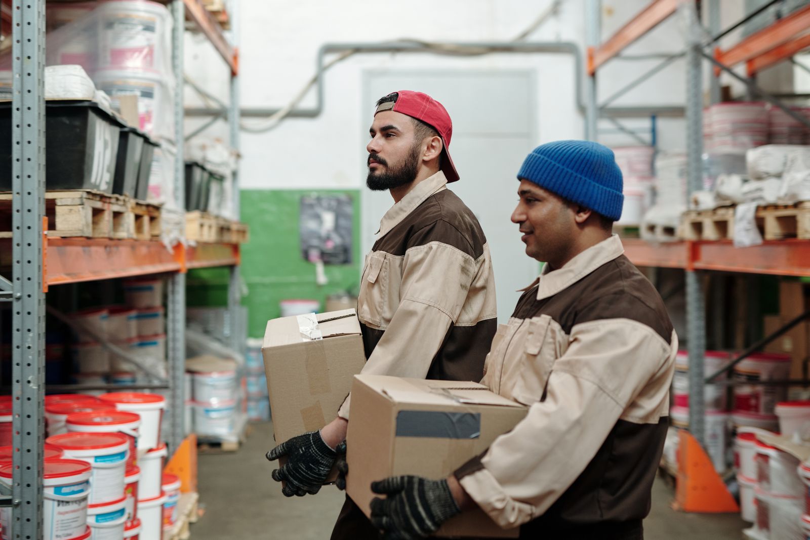 Two warehouse workers carrying cardboard cartons along storage racks